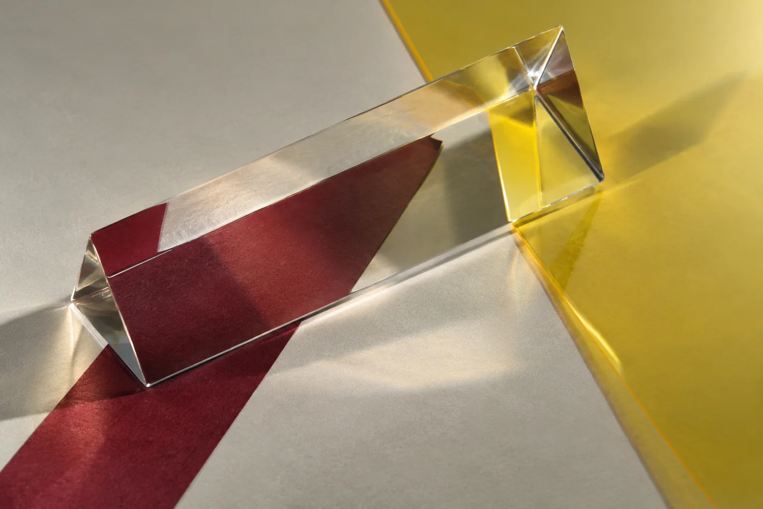 Clear glass prism resting above separate yellow and burgundy paper planes